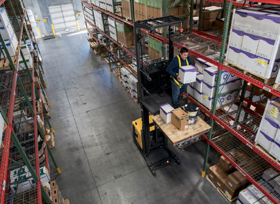 Worker strapped to raised platform of a Cat High-Level Order Picker to reach high shelf